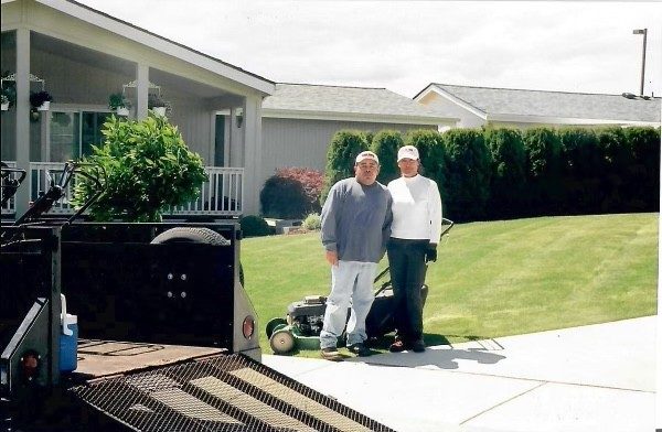 The owners standing beside their mower and trailer in front of a finished lawn